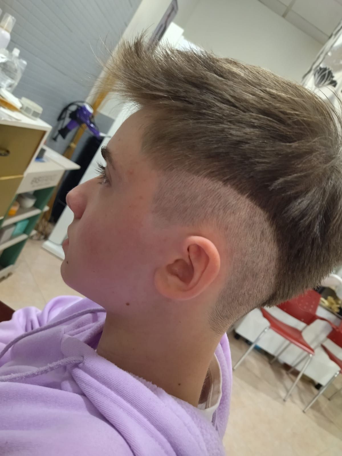 Niño con corte de pelo moderno, perfil lateral, cabello castaño claro, laterales descoloridos, en interior.