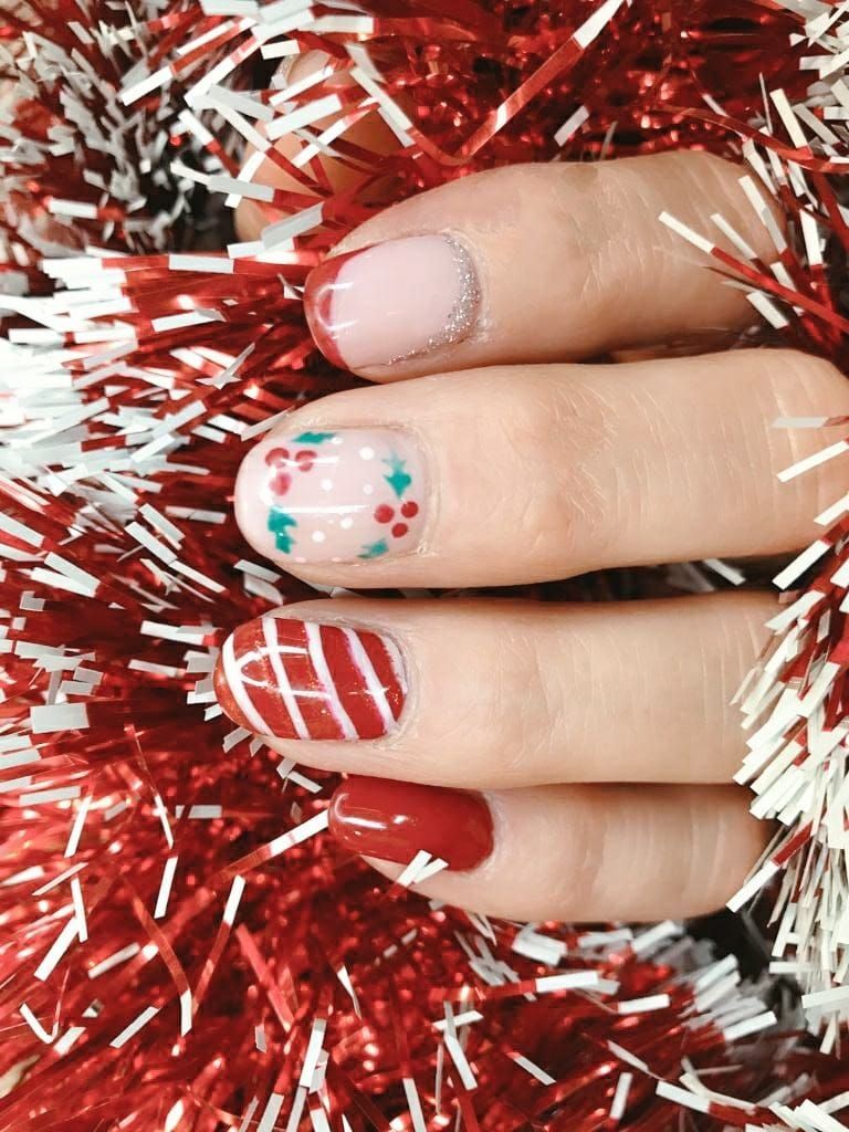 Uñas festivas con diseños festivos: cuadros rojos y blancos, puntos y acebo, rodeados de oropel rojo y blanco.