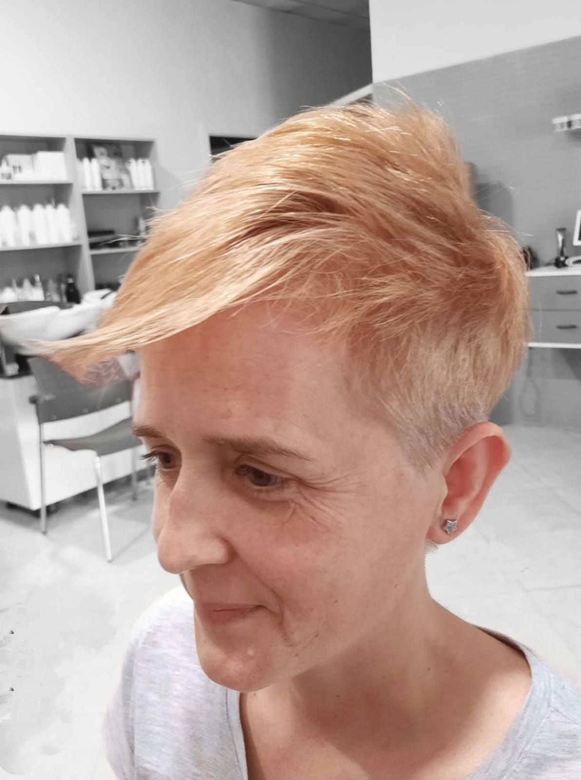 Mujer con cabello corto de color naranja claro. Vista de perfil, sonriendo levemente, en un salón de belleza.