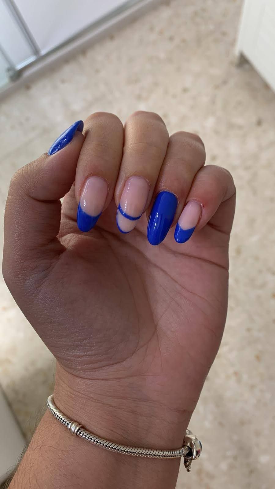 Mano con uñas de punta francesa azules y blancas, luciendo una pulsera de plata.