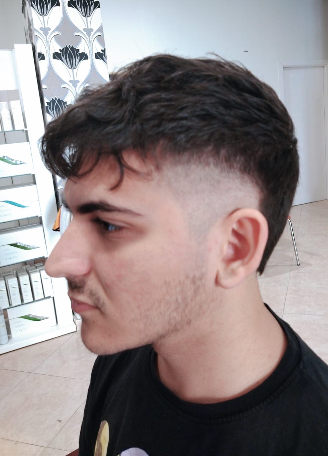 Hombre con corte de pelo descolorido mirando hacia la izquierda, vistiendo una camisa negra.