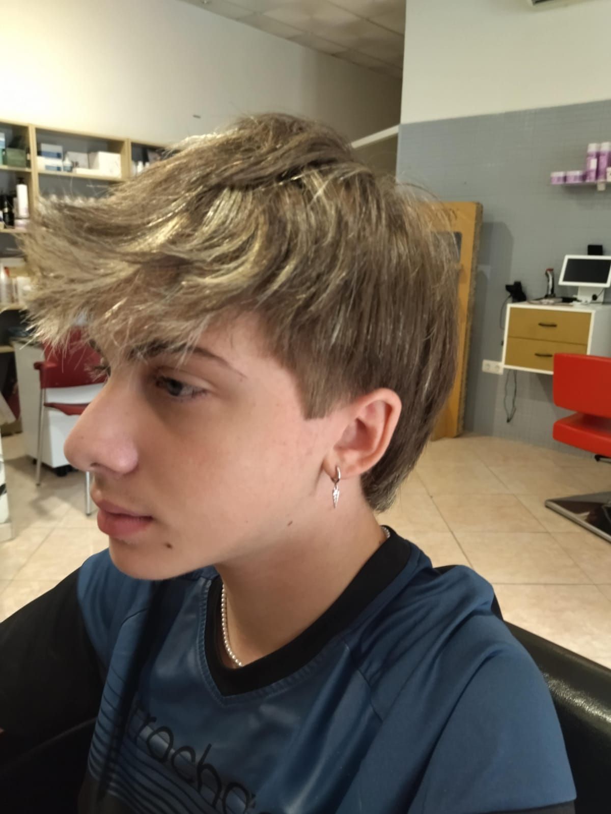 Persona joven con cabello castaño claro y texturizado, vestida con una camisa azul, en un salón de belleza.