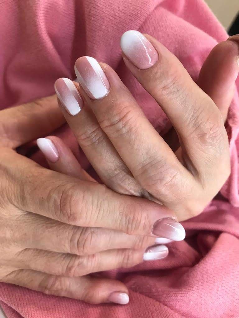 Manos con uñas de forma ovalada que presentan un diseño ombré de color rosa a blanco.