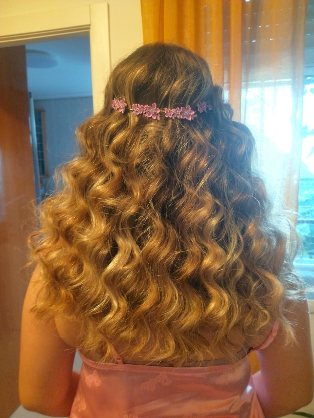 Mujer con cabello rubio largo y rizado, con un vestido rosa y una diadema floral rosa.