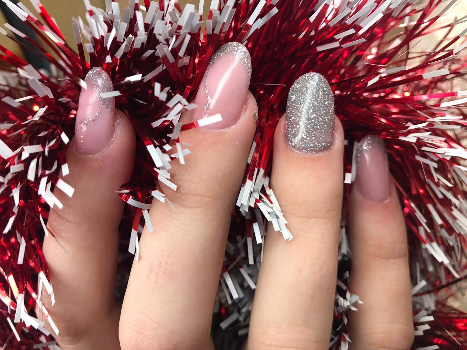 Mano con uñas largas y esmaltadas en color rosa y brillo sobre fondo rojo y blanco.