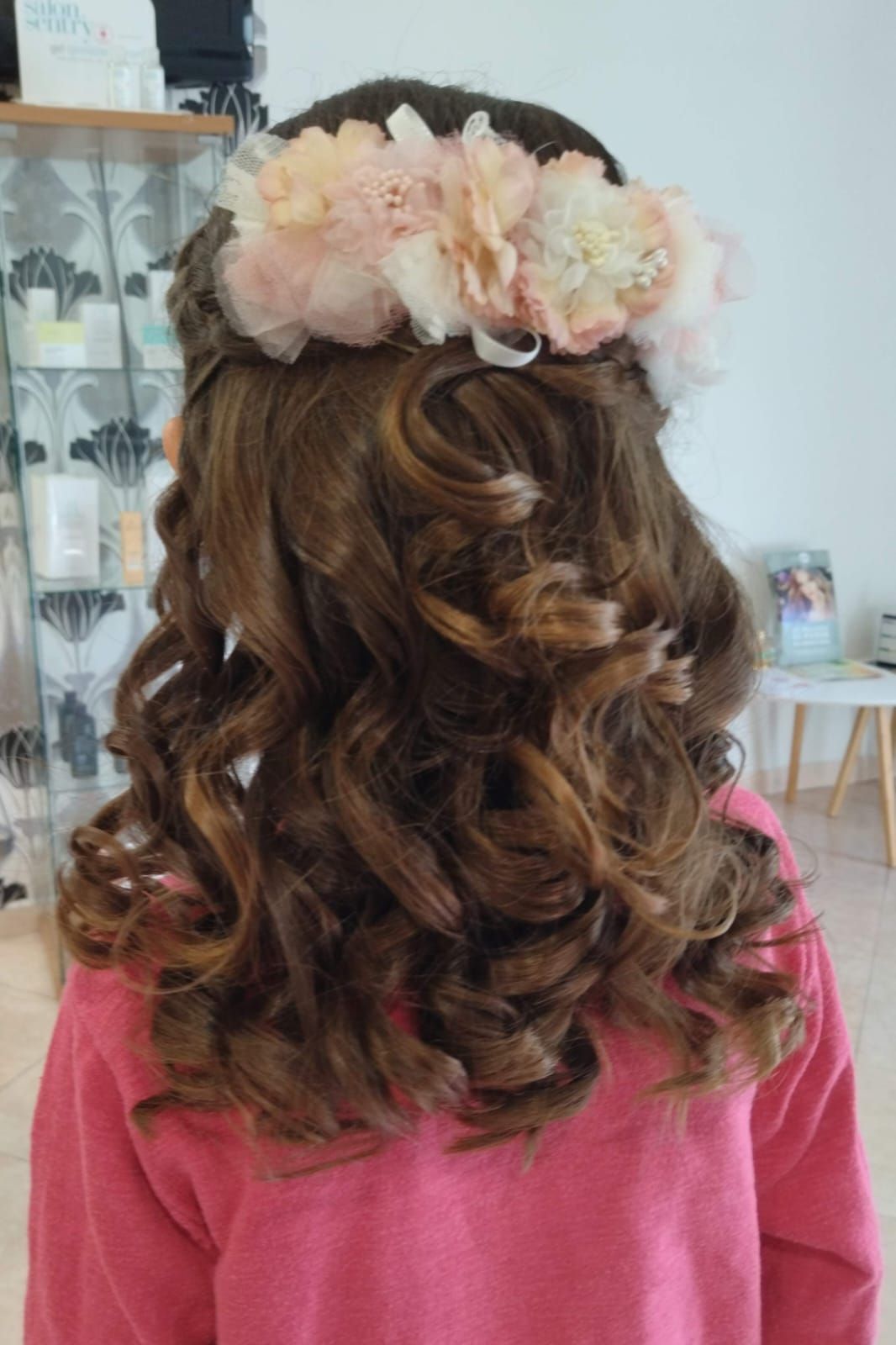 Chica con cabello castaño y rizado, con una corona de flores, en un salón.