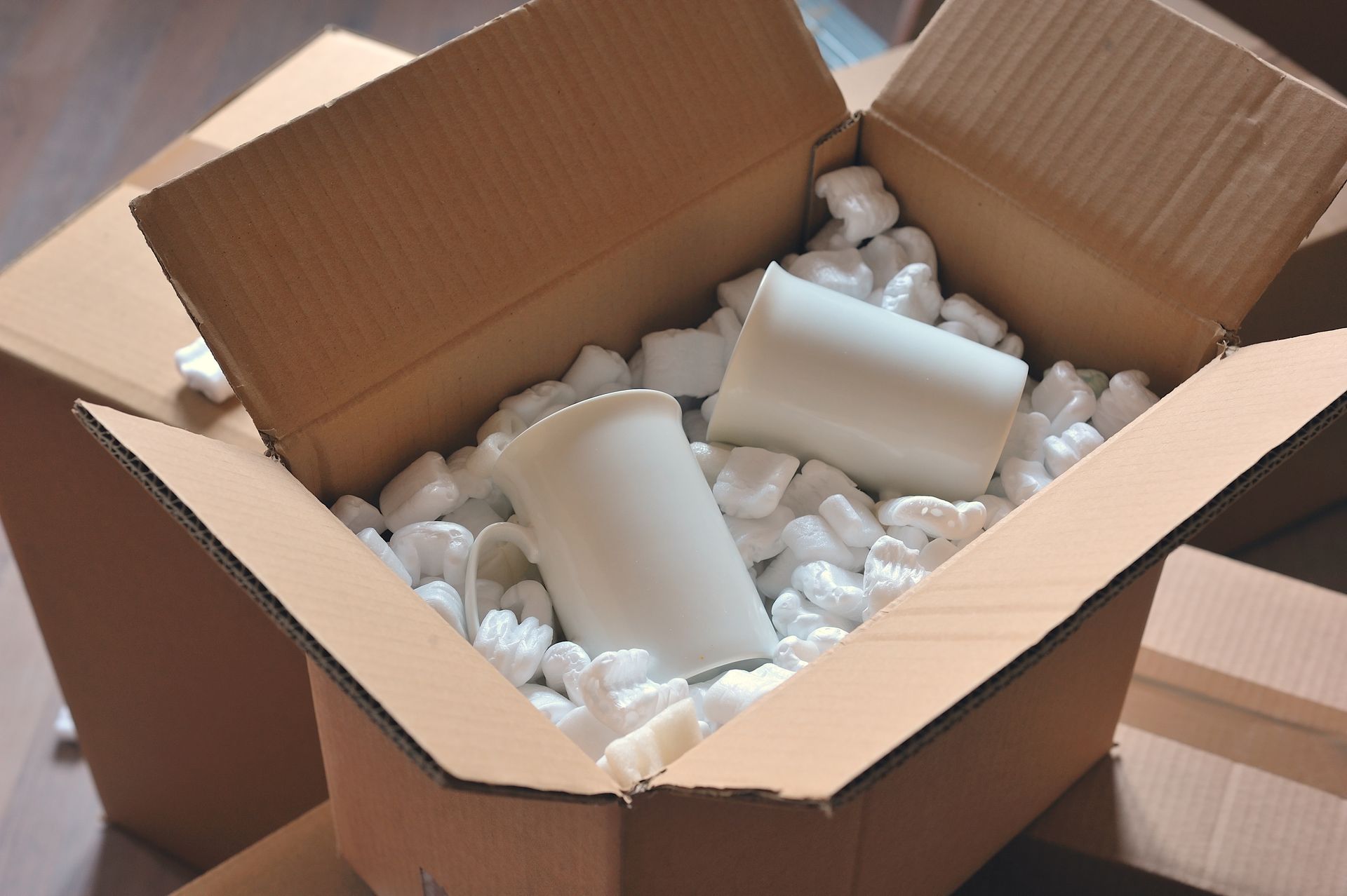 Un carton ouvert contenant deux tasses et des copeaux de polystyrène