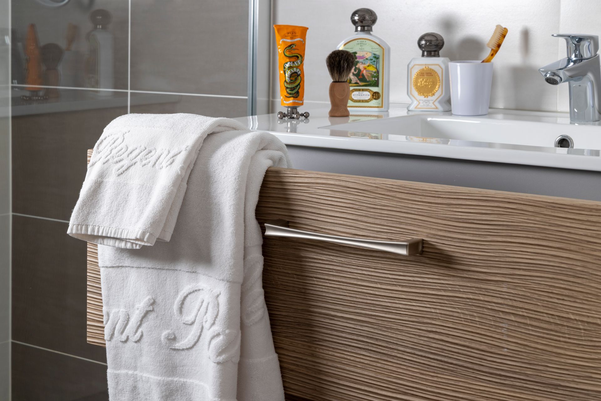 Une serviette blanche est drapée sur un meuble texturé, des articles de toilette étant posés sur le comptoir de la salle de bain.