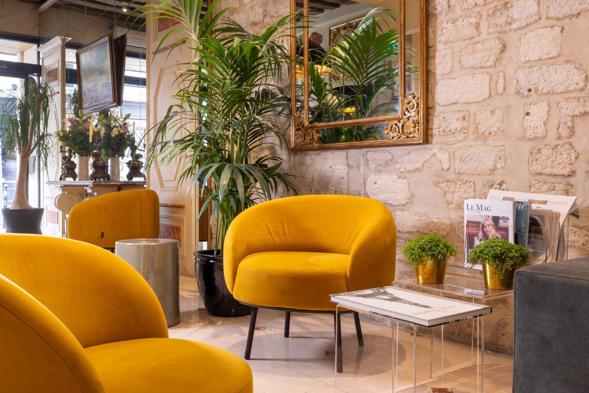 Coin salon cosy avec fauteuils en velours jaune, plantes, mur de briques apparentes et miroir orné à cadre doré.