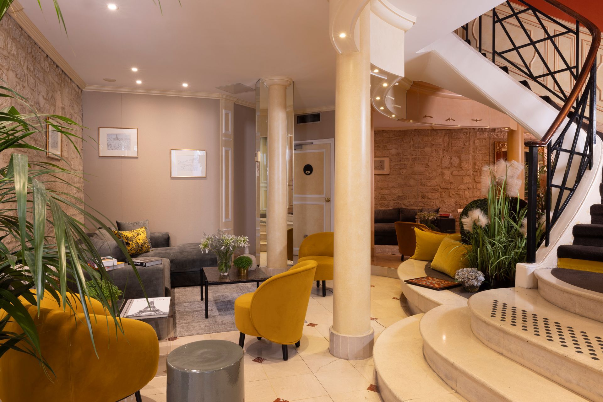 Hall d'hôtel avec chaises jaunes, canapé gris et escalier en colimaçon.