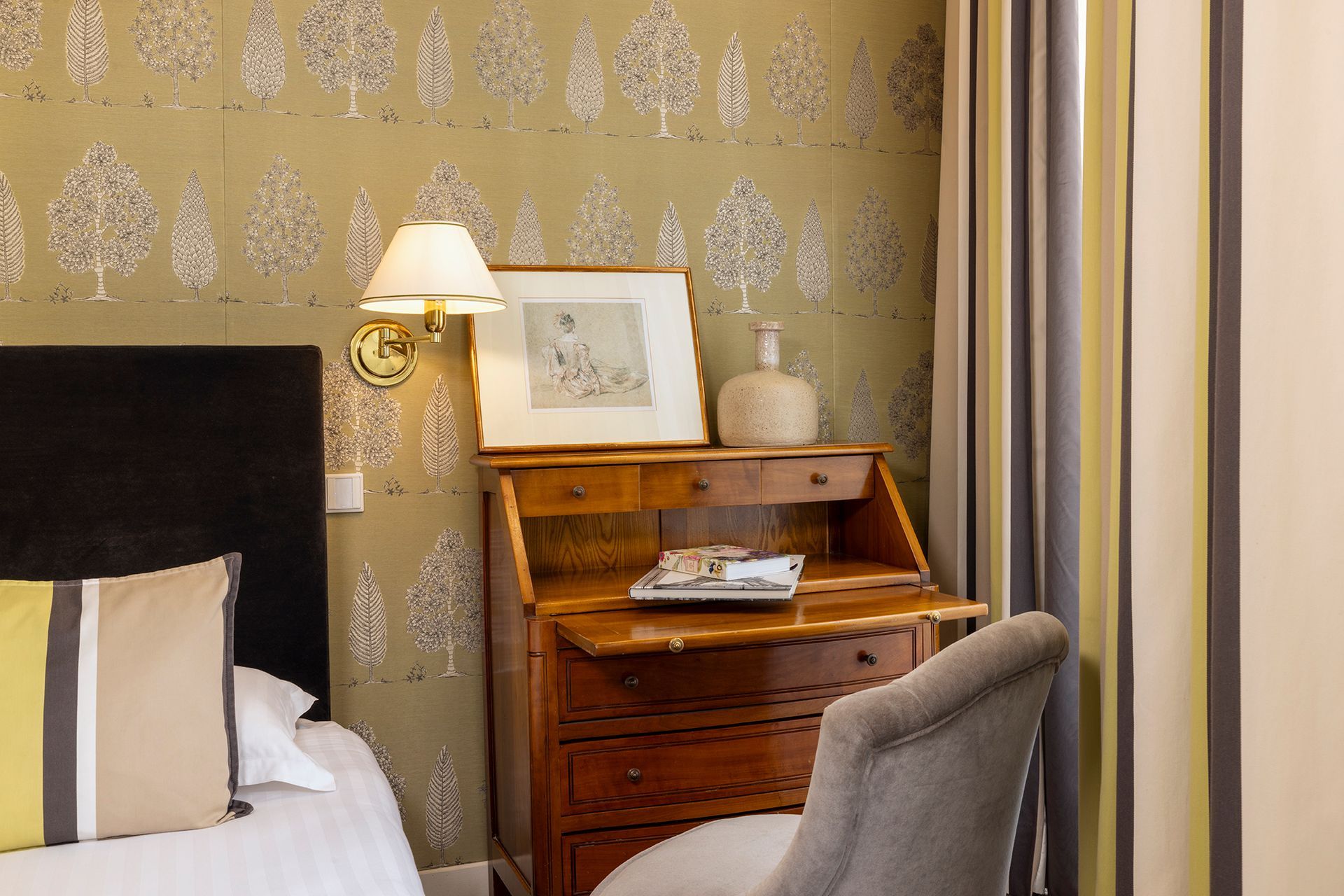 Chambre avec bureau, papier peint à motifs d'arbres, lit avec oreillers et applique murale.