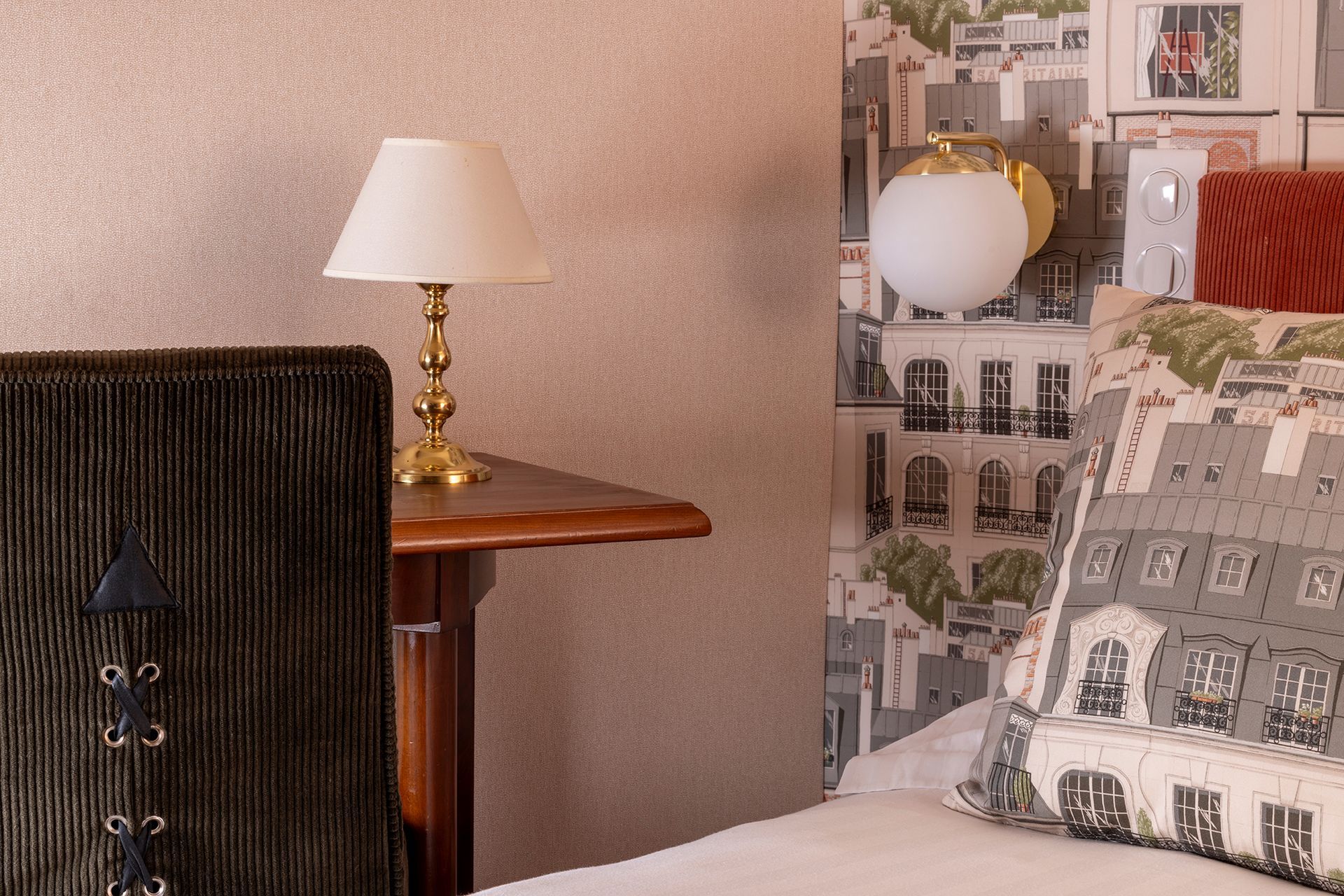 Un coin de chambre avec une lampe sur une petite table, un lit avec un oreiller et une applique murale.