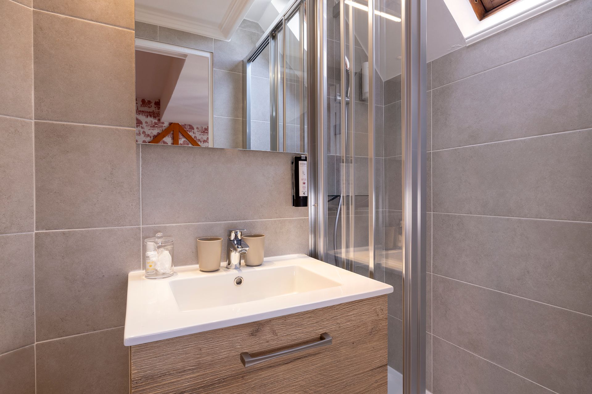 Salle de bains avec meuble-lavabo et douche en verre. Les murs sont carrelés de beige. Un miroir est accroché au-dessus du lavabo.