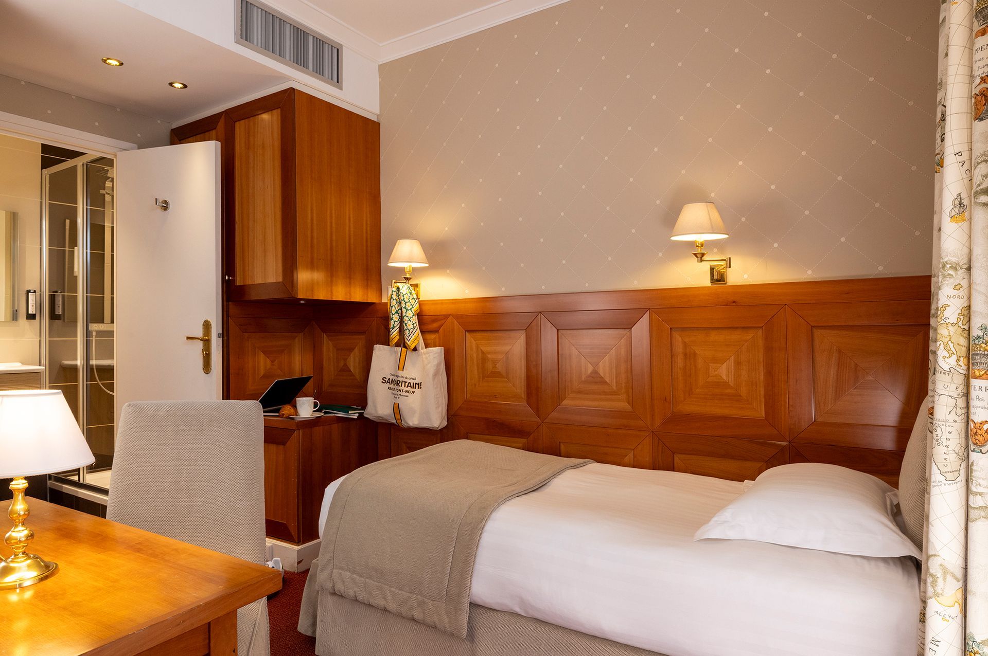 Chambre d'hôtel confortable avec un lit simple, des boiseries, un bureau et une salle de bains partiellement visible.