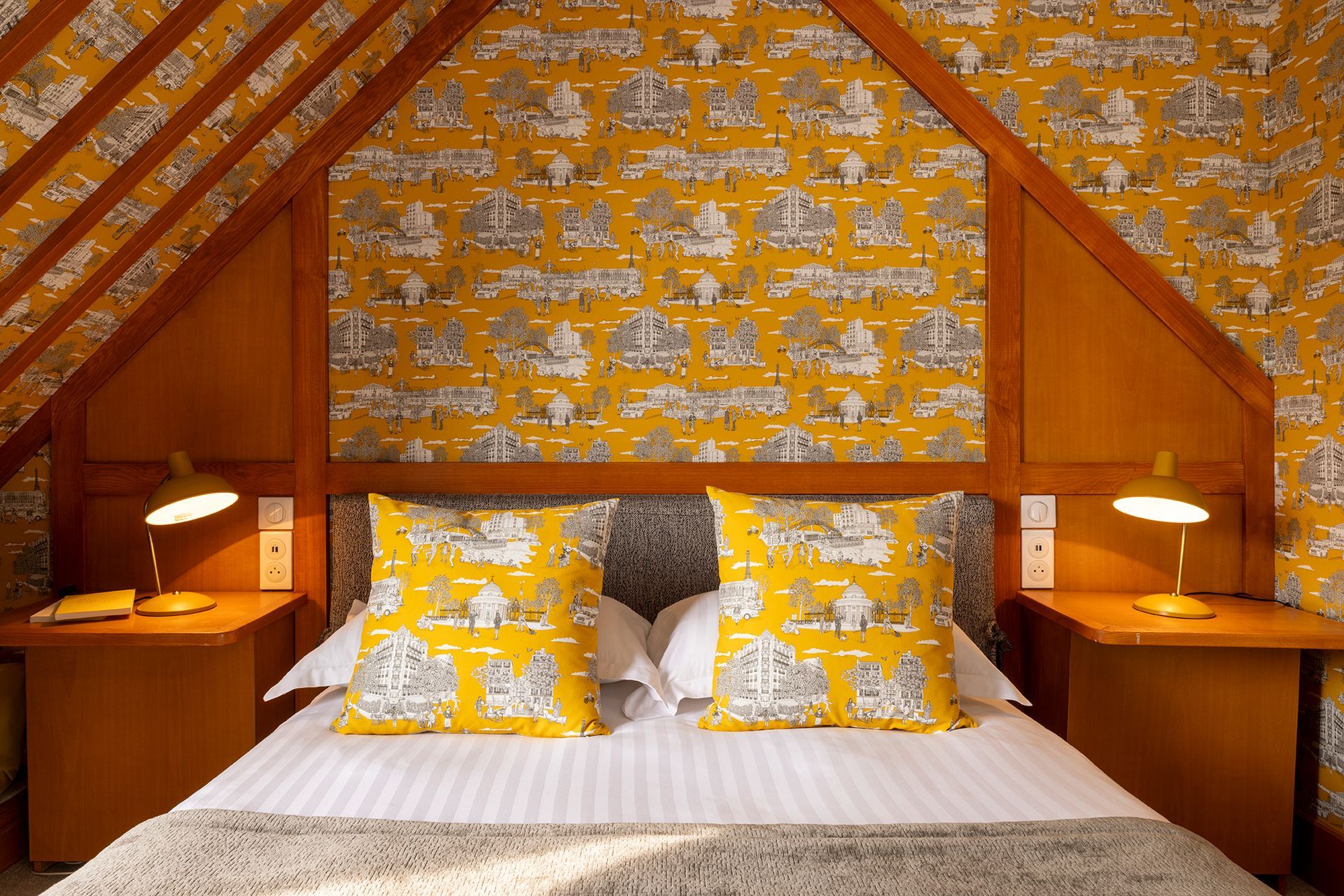 Chambre avec papier peint à motifs jaunes, lit avec oreillers assortis et tables de chevet avec lampes.