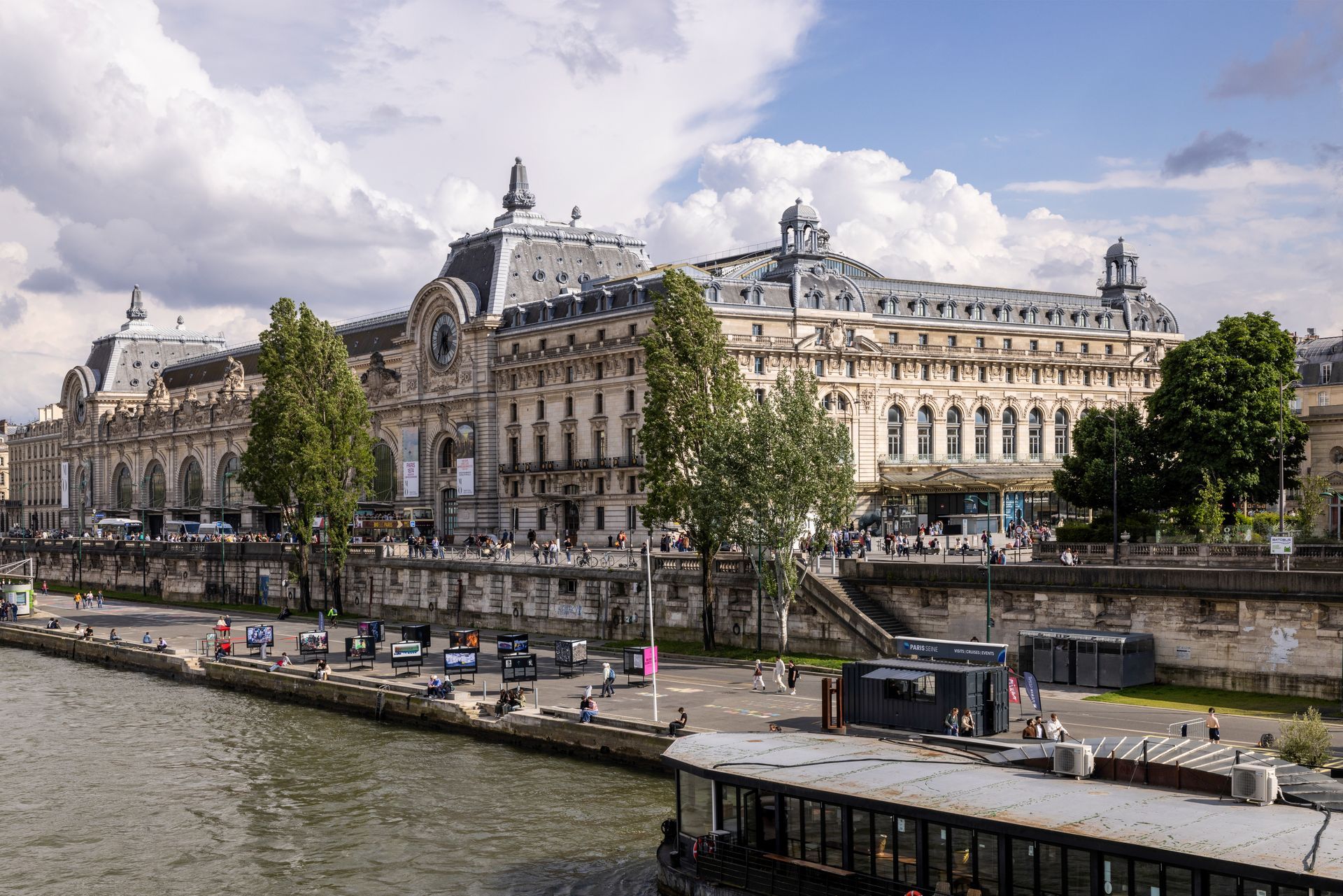 Extérieur du musée d'Orsay, à Paris, vu depuis la Seine. Bâtiment orné à la façade de pierre, sous un ciel nuageux.