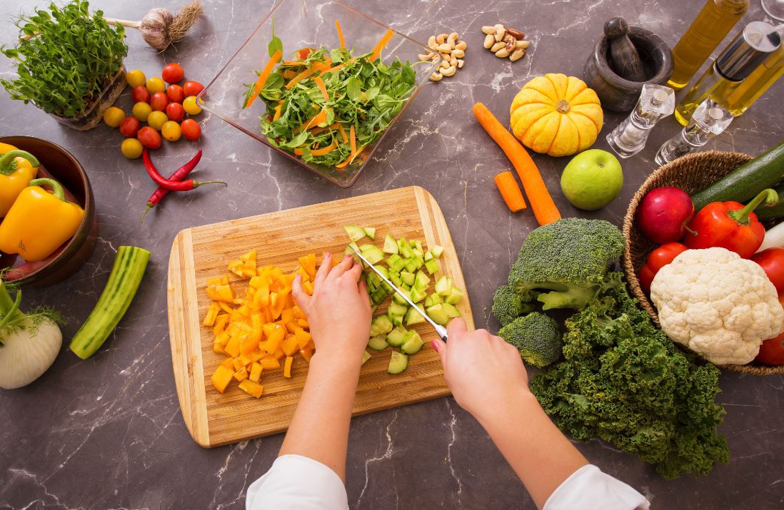 Personne en train de couper des légumes sur une planche à découper, autres légumes posés sur le plan de travail