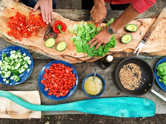 Deux personnes en train de cuisiner des légumes sur un plan de travail en bois naturel