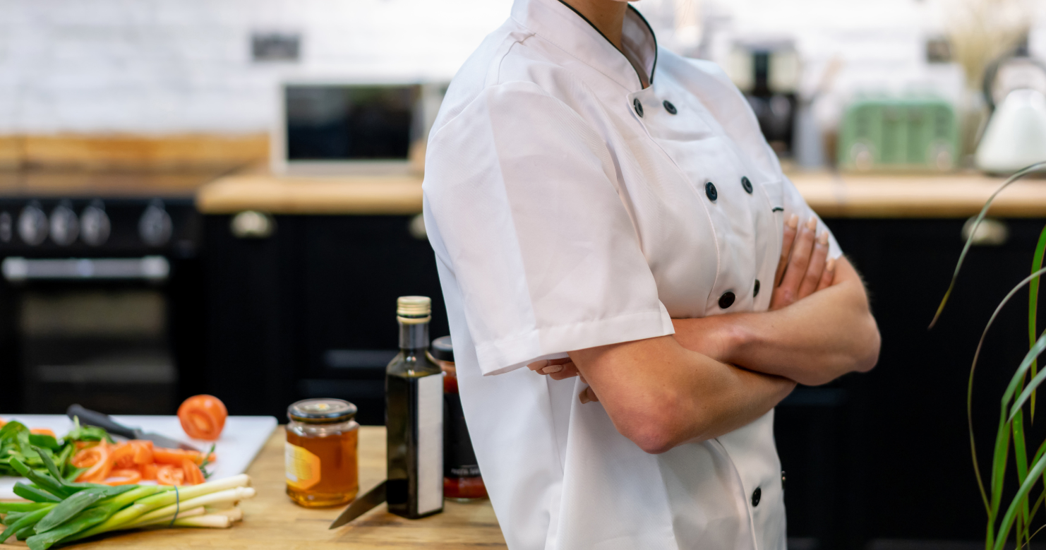 Chef cuisinier debout les bras croisés devant un plan de travail avec plusieurs ingrédients posés dessus