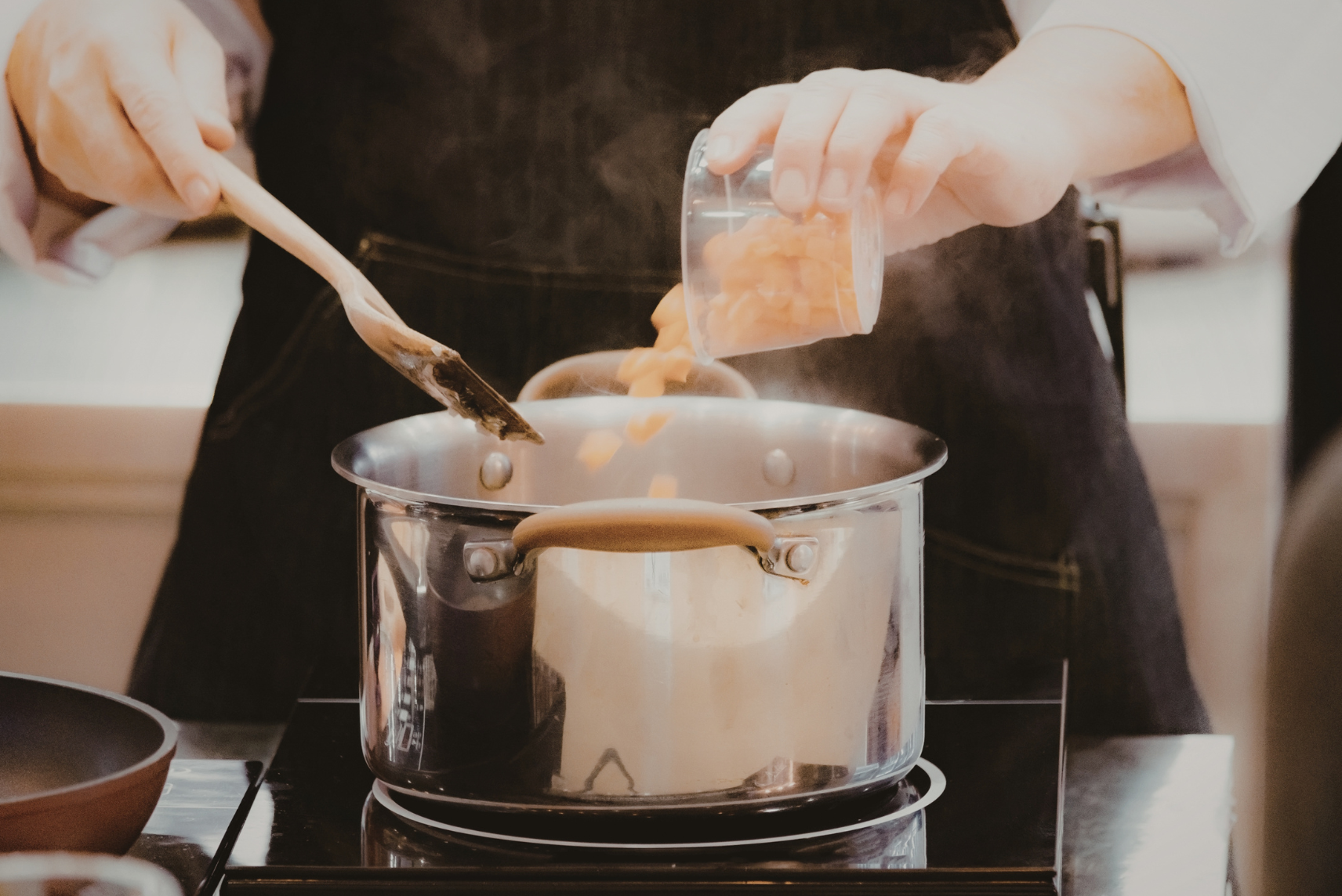 Personne versant un contenant dans une casserole et tenant une cuillère en bois