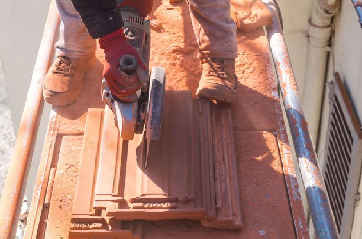 Ouvrier utilisant une scie électrique pour découper un panneau de bois sur un chantier de toiture