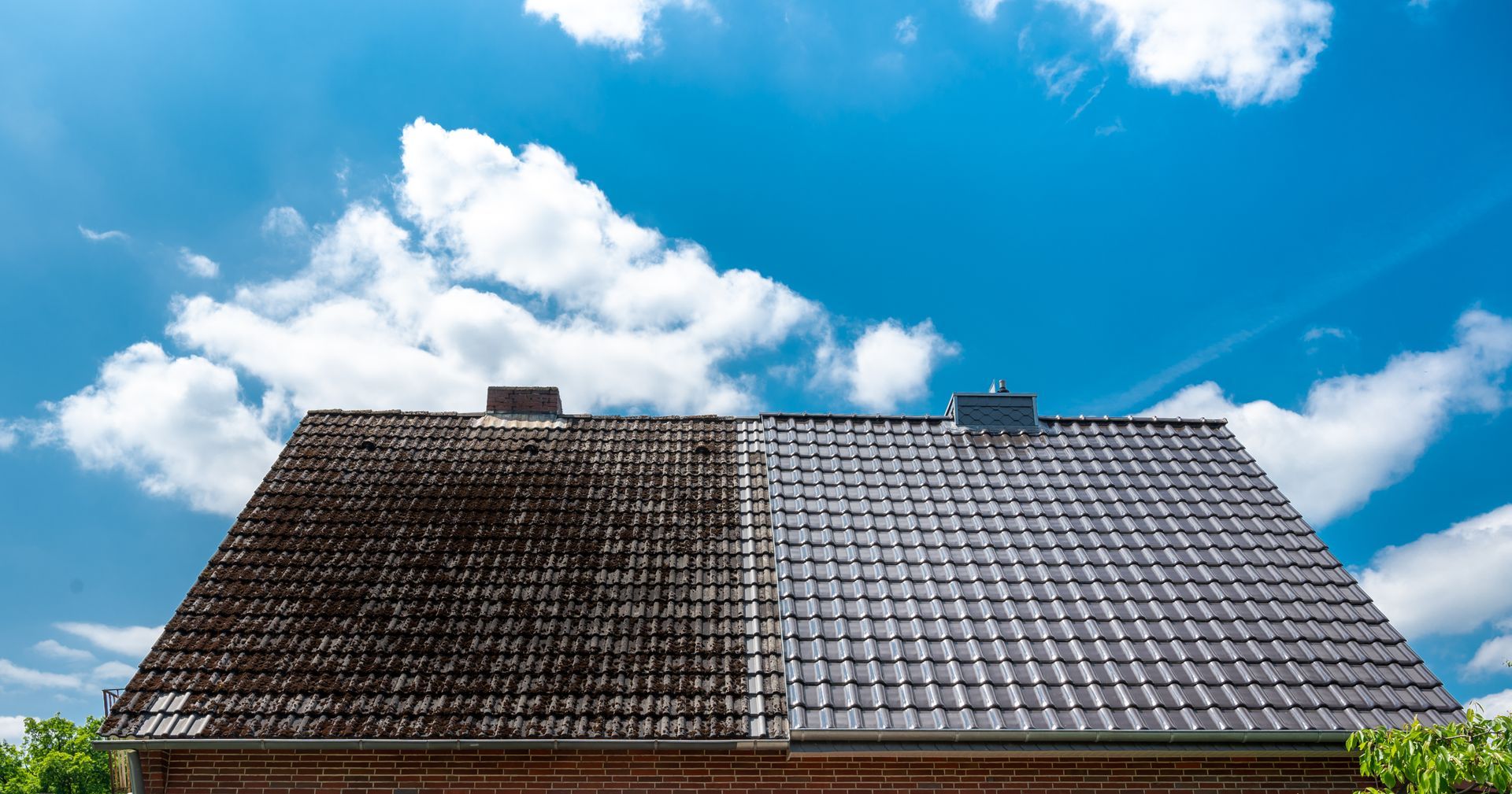 Toit de maison aux tuiles de deux couleurs différentes sous un ciel bleu vif parsemé de nuages