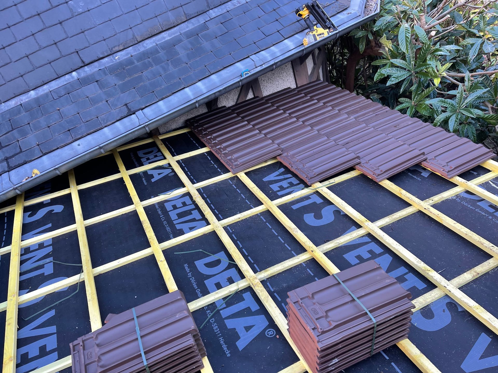 Toiture en construction avec membrane d'étanchéité noire, quadrillage jaune et bardeaux bruns empilés en bordure.