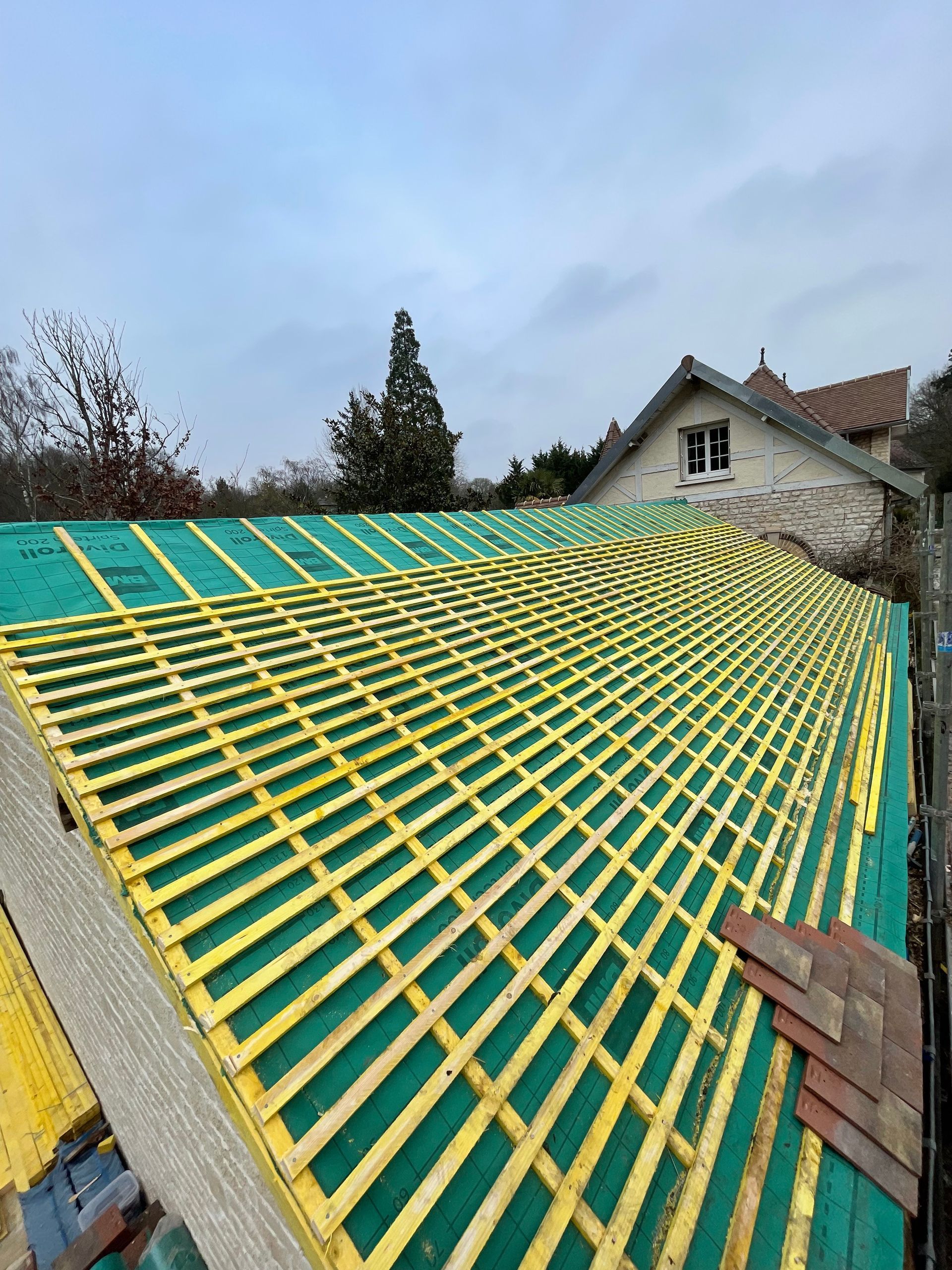 Toiture en construction avec membrane d'étanchéité verte et liteaux en bois jaunes sur une maison