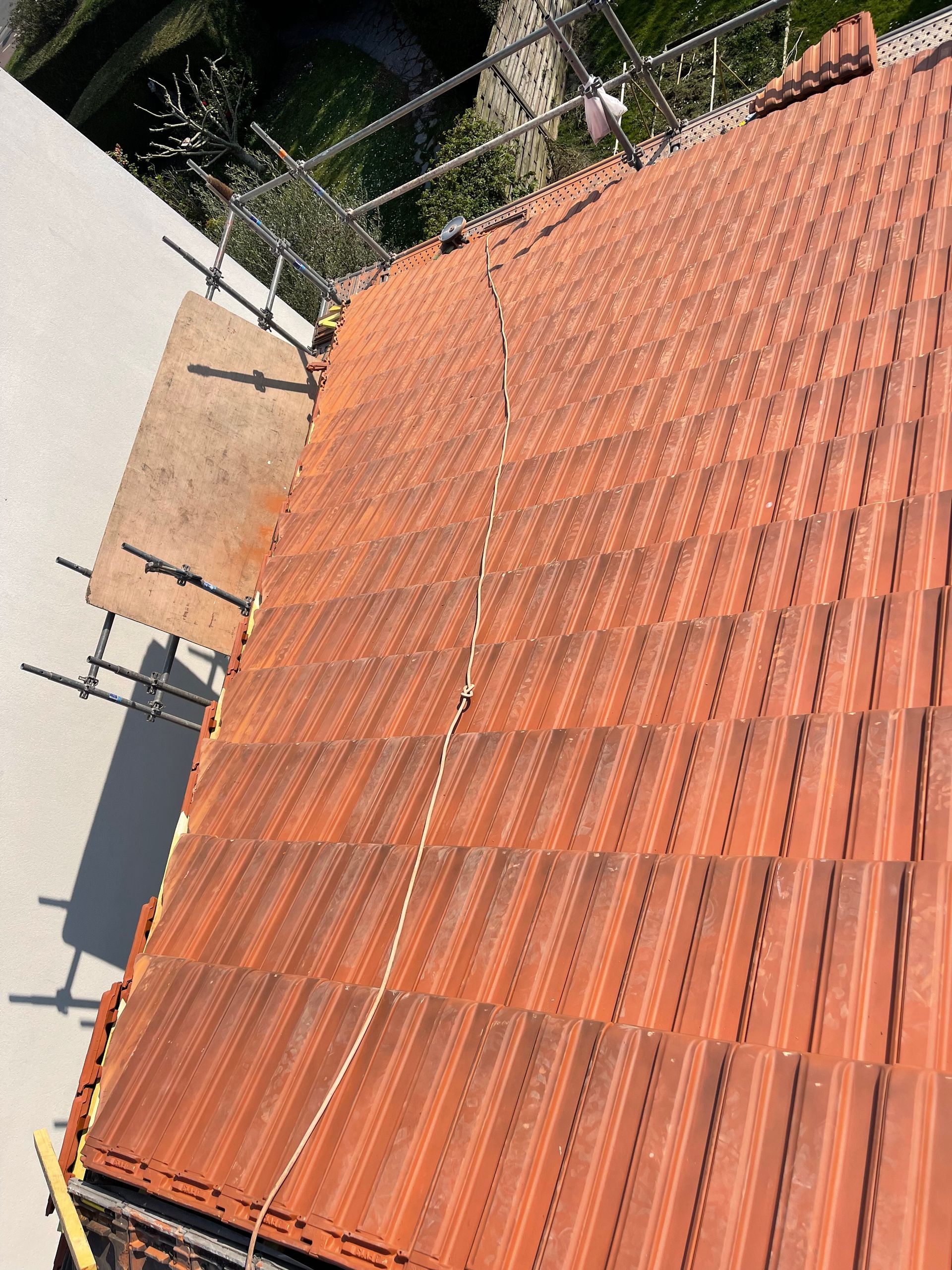 Toit de tuiles orange à côté d'un mur blanc et d'arbres, vu d'en haut en biais