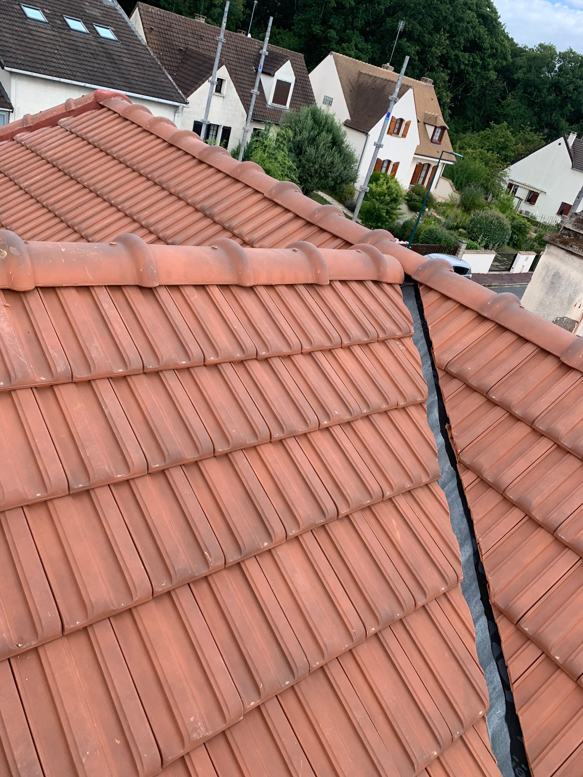 Toiture en tuiles rouges avec solins noirs, donnant sur les maisons et les arbres voisins