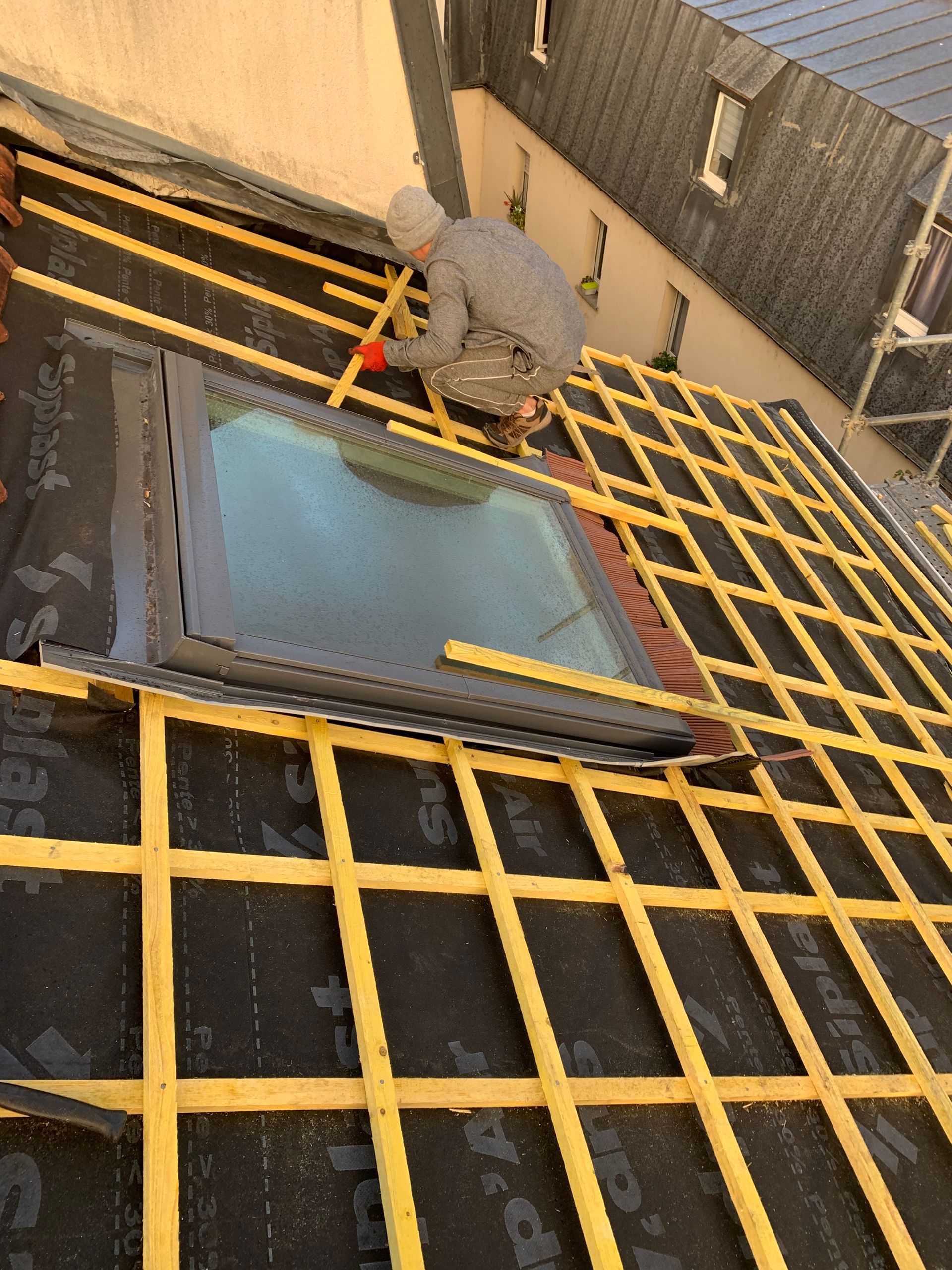 Ouvrier utilisant un outil sur une grille jaune au-dessus d'une grande ouverture rectangulaire dans un environnement industriel