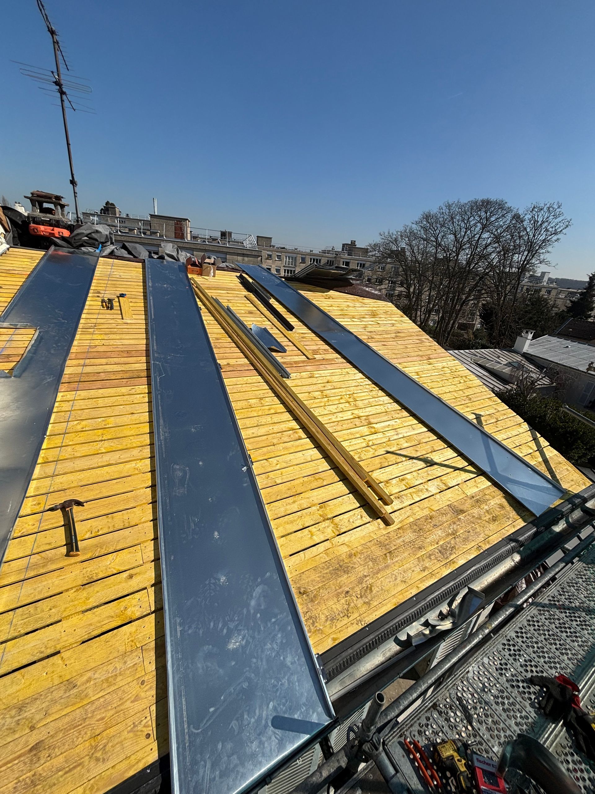 Rampe métallique jaune et bleue en construction sur un toit, avec des arbres et un ciel bleu en arrière-plan.