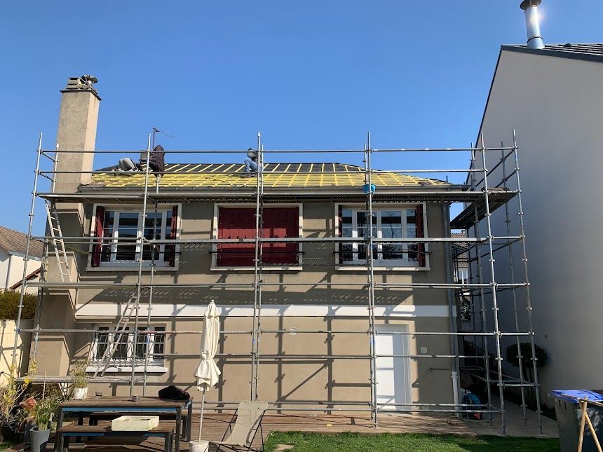 Façade d'une maison en rénovation, avec échafaudages et bordure de toit métallique sur fond de ciel bleu.