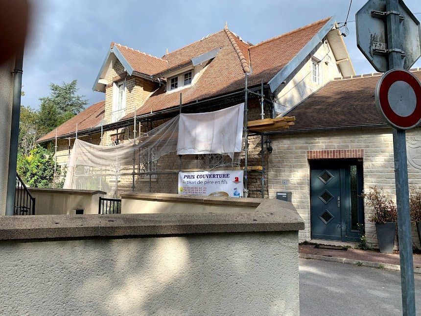 Ancien bâtiment en briques avec un toit de tuiles rouges, des bannières et un panneau de rue en façade