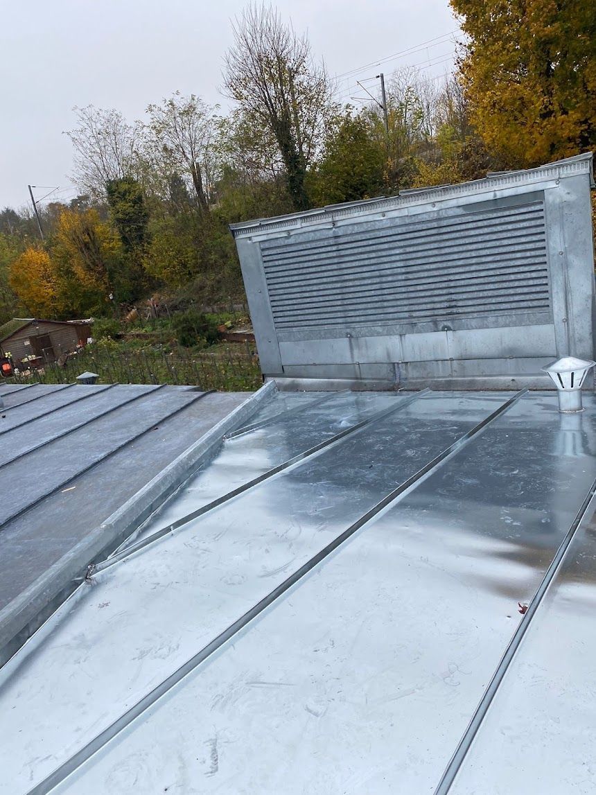 Toit en métal brillant avec une grille d'aération surélevée, encadré par des arbres d'automne en arrière-plan