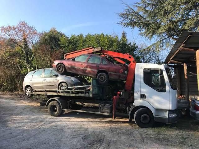 Une dépanneuse charge deux voitures endommagées sur un parking, une berline rouge empilée au-dessus d'une voiture à hayon argentée.