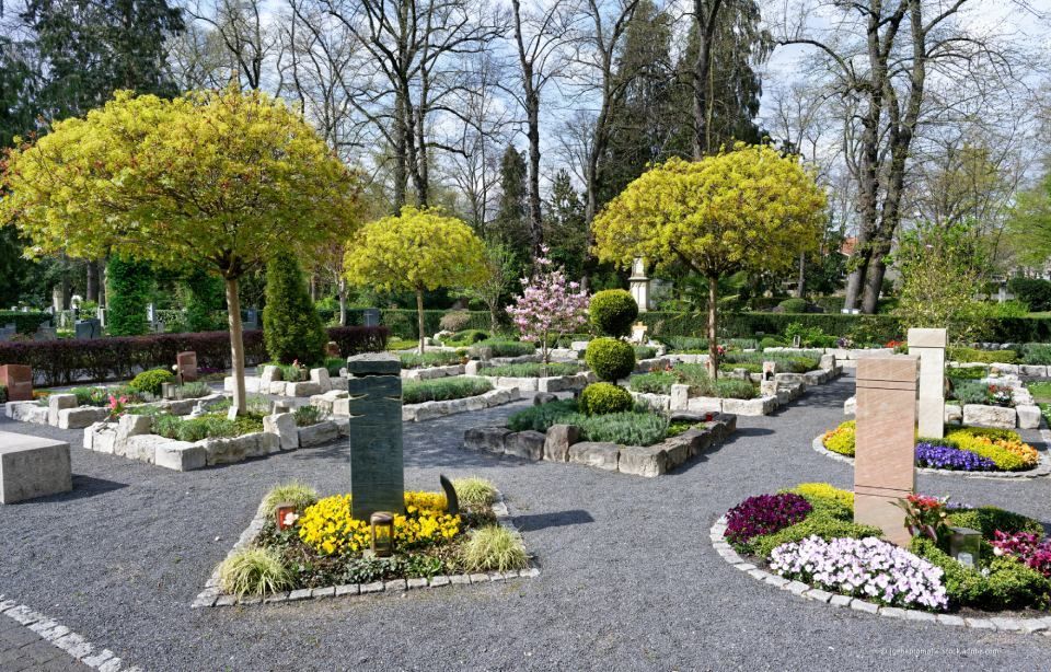 Landschaftlich gestalteter Garten mit Blumenbeeten, Kieswegen und im Frühling blühenden, beschnittenen Bäumen