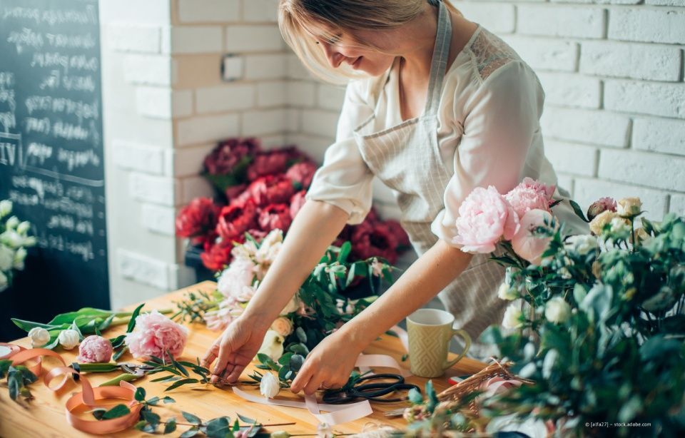 Floristin arrangiert Blumen auf einem Holztisch in einer hellen Werkstatt