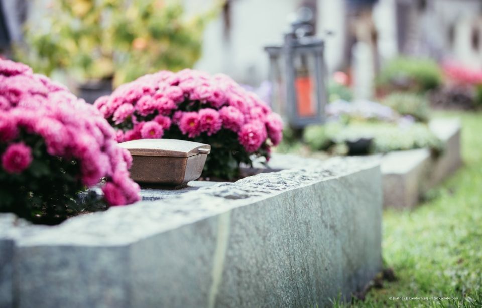 Rosa Blumen auf einem Granitgrabstein auf einem Friedhof, daneben eine kleine Laterne.