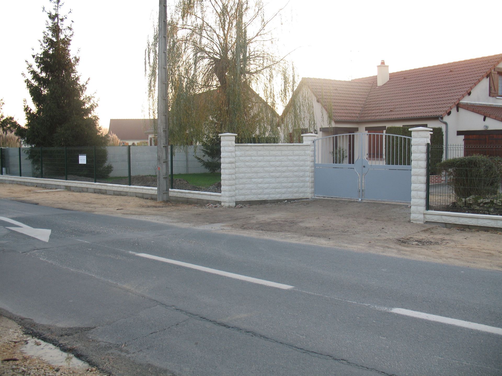 Une maison avec une clôture en briques et une allée dans une rue.
