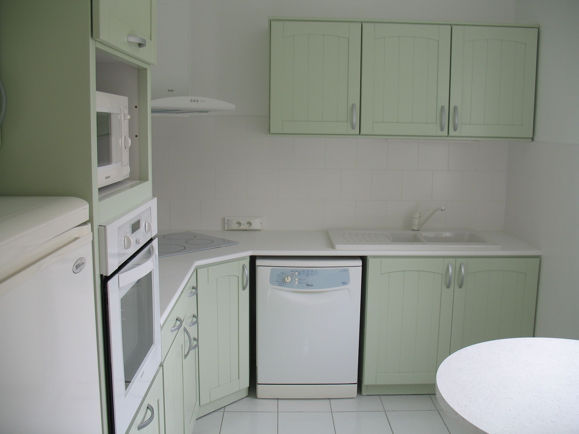 Petite cuisine avec des armoires vertes, des appareils blancs et une table ronde.