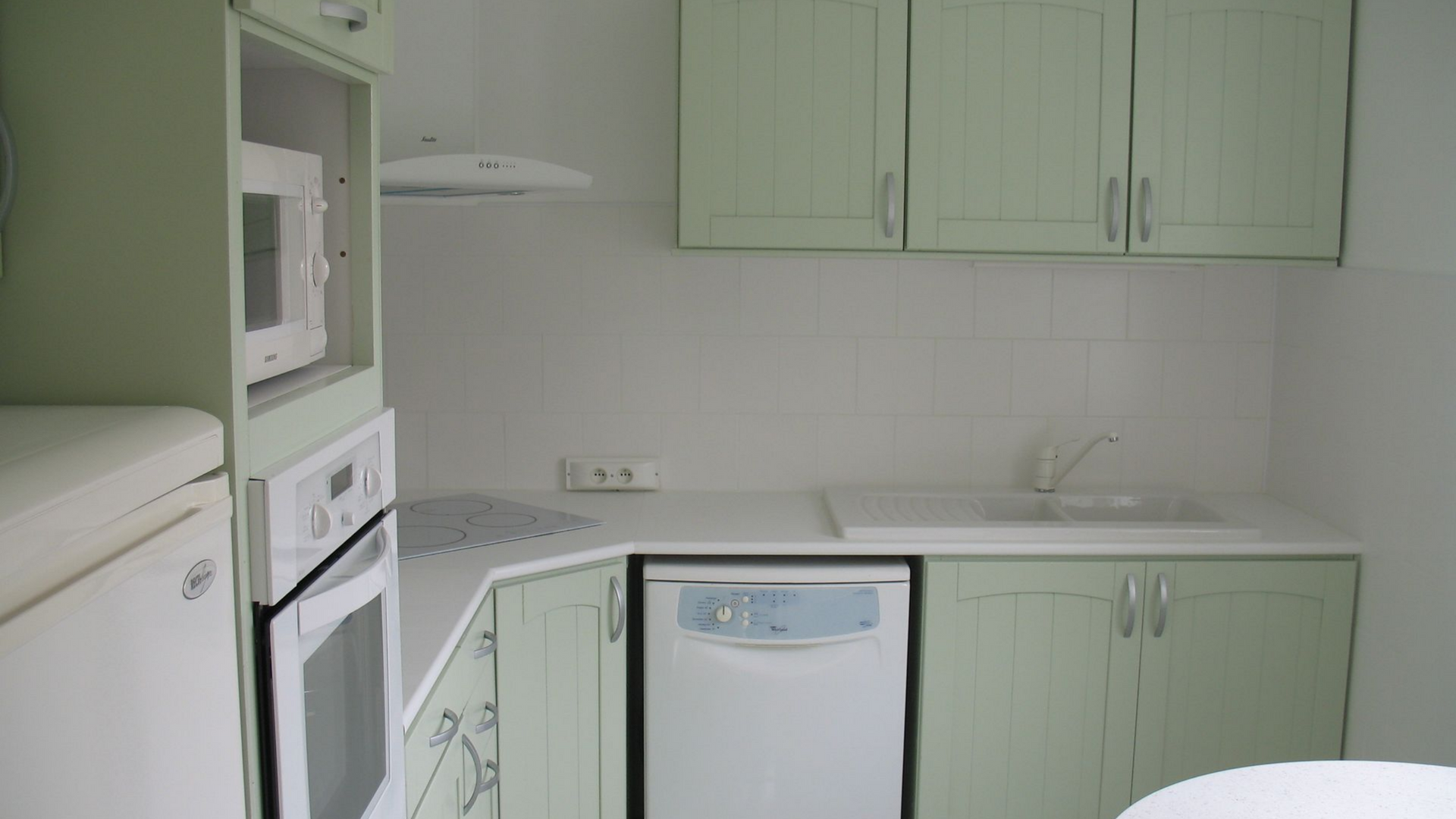 Petite cuisine avec des armoires vert menthe, des appareils électroménagers blancs et un comptoir blanc.