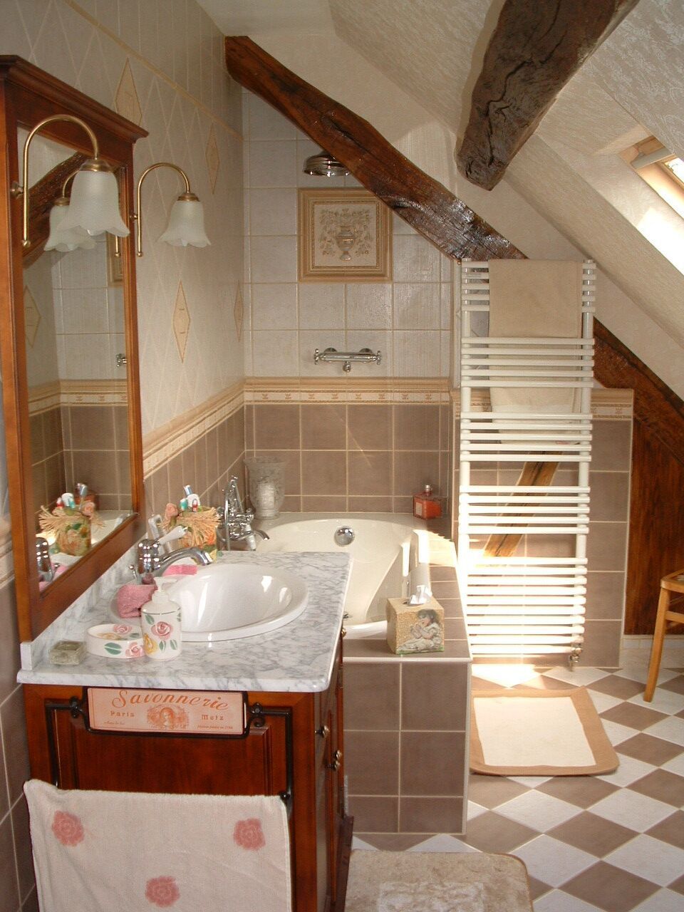 Salle de bains avec carrelage marron et crème, vanité en bois et plafond en pente avec poutres apparentes.