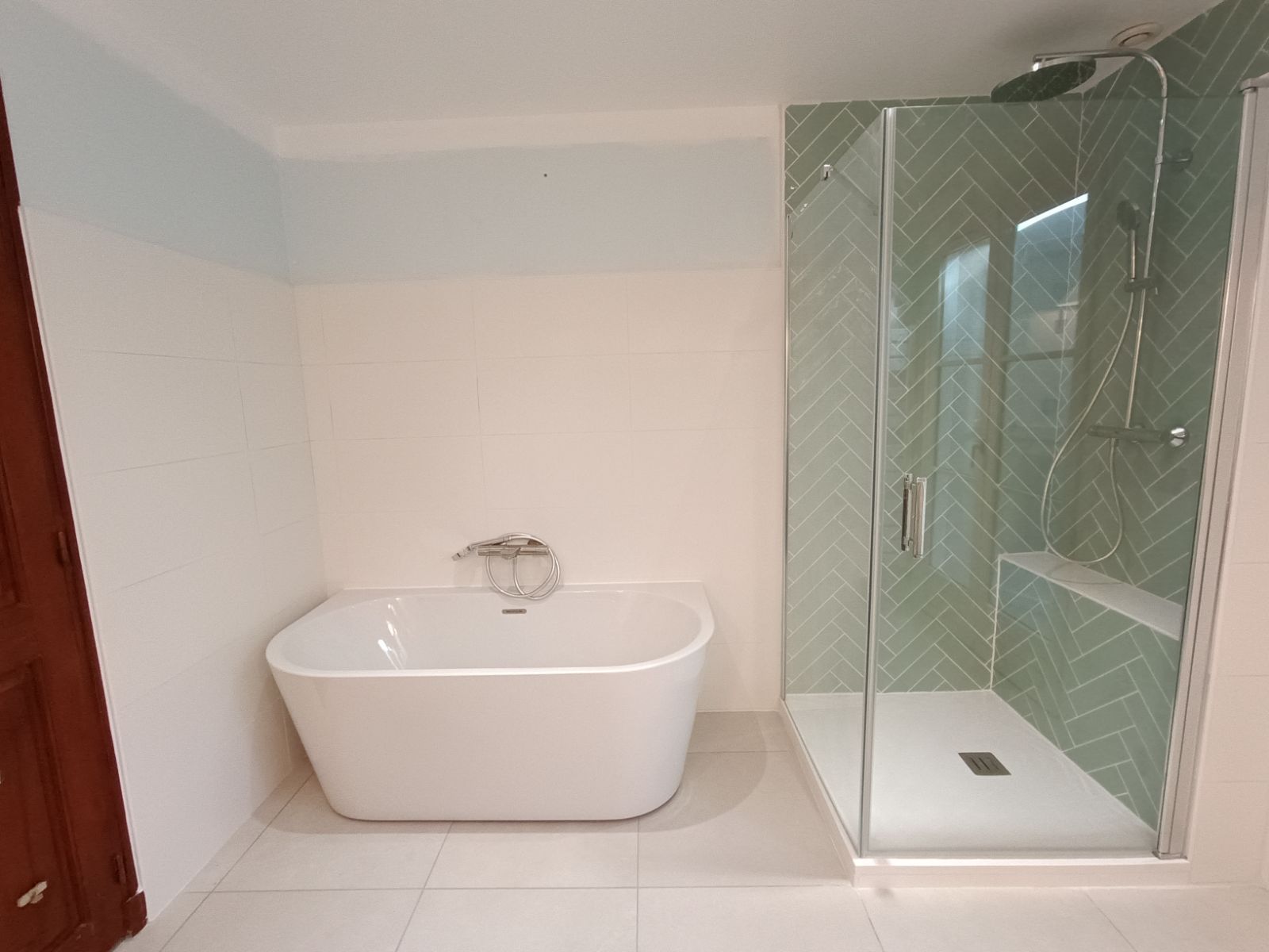 Salle de bain moderne avec baignoire blanche, douche en verre et carrelage vert.