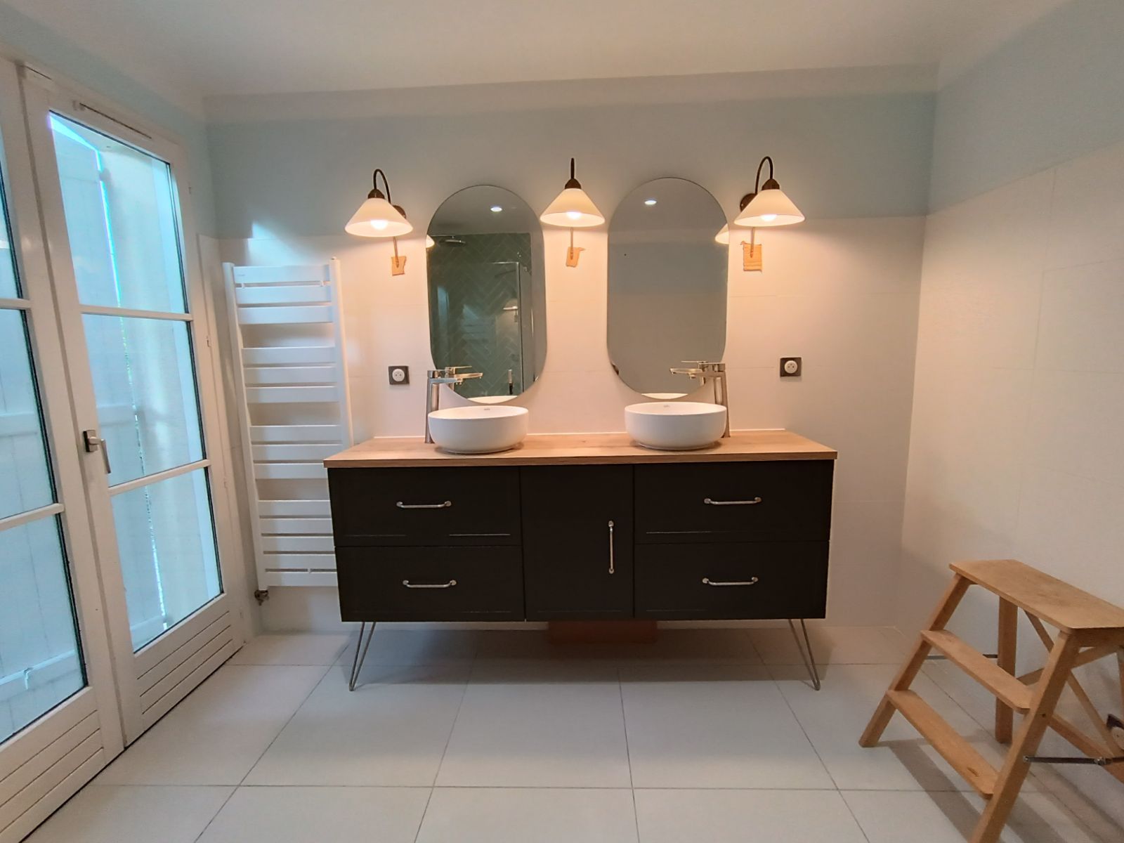 Salle de bain avec double vasque, deux miroirs et appliques, dans une pièce bleu clair et blanche.