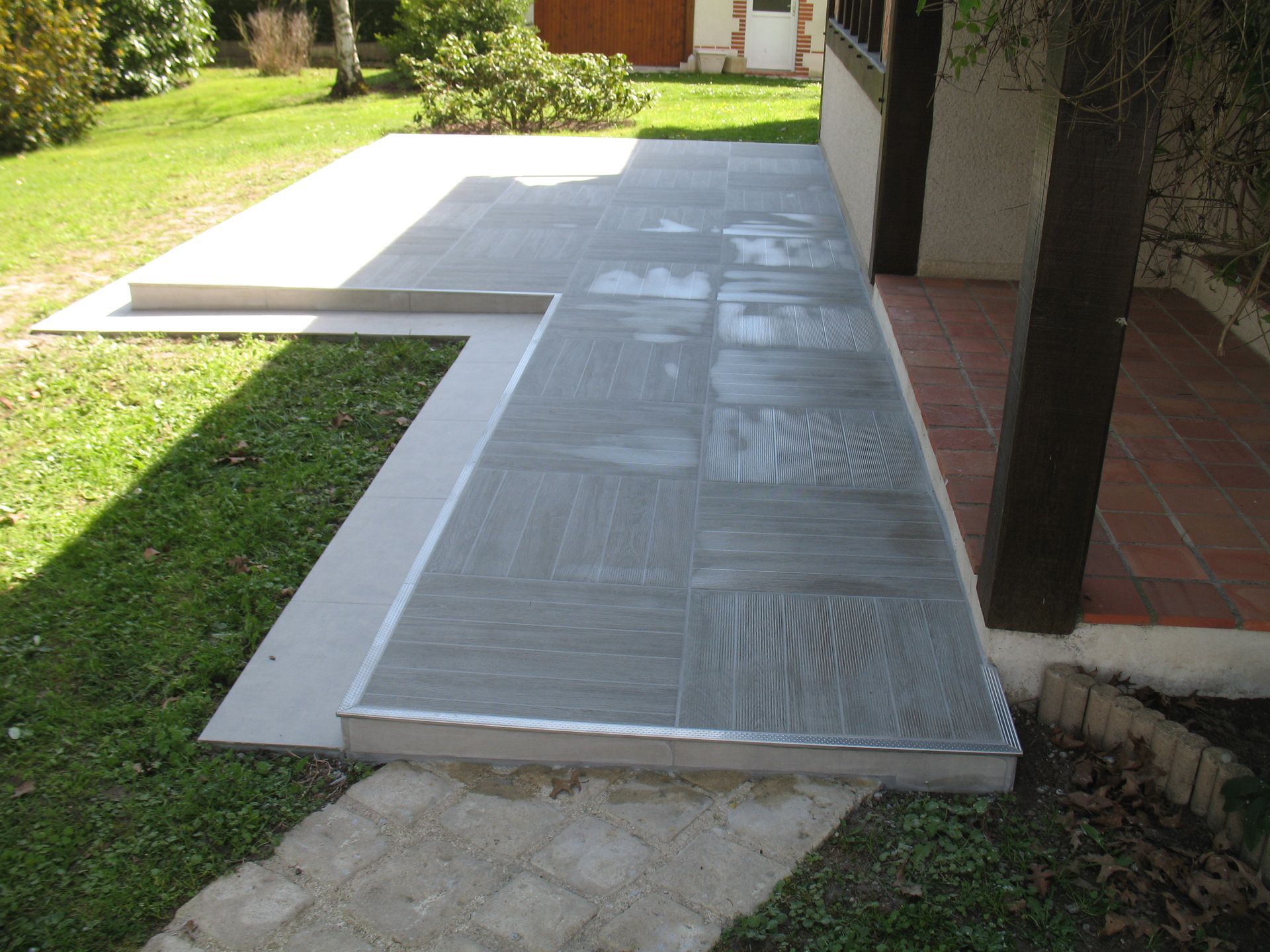 Terrasse carrelée grise avec une marche, à côté d'un bâtiment, menant à l'herbe.