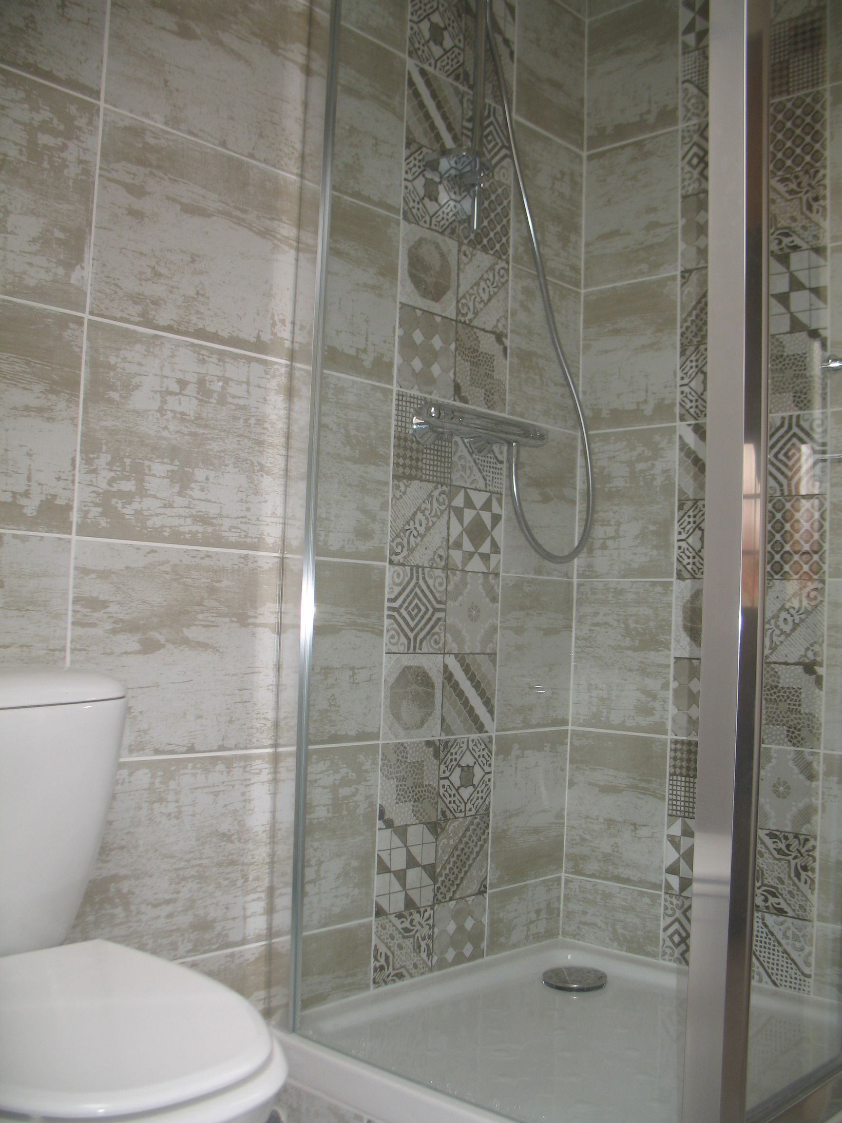 Cabine de douche avec murs carrelés à motifs et toilettes.