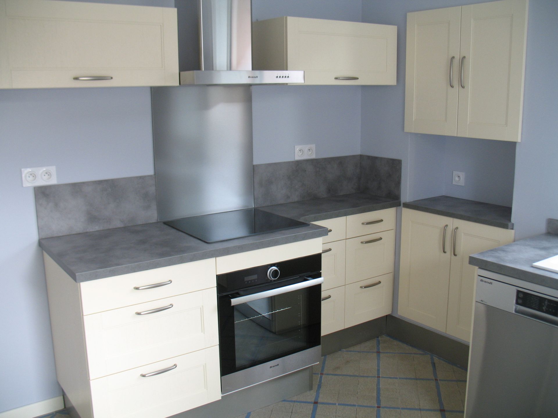 Armoires de cuisine couleur crème avec comptoirs et crédence gris. Four et table de cuisson intégrés.