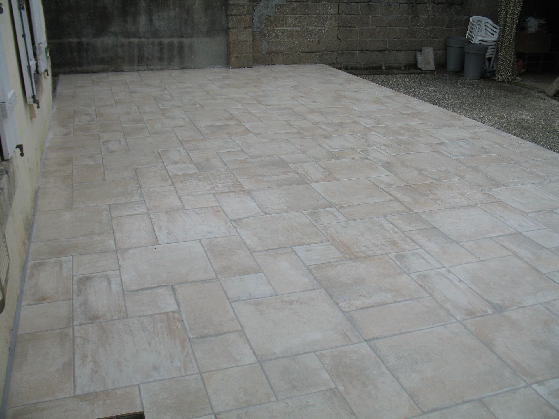 Terrasse en pierre beige. Dalles rectangulaires variées disposées de façon aléatoire. Extérieur, à côté d'un bâtiment.