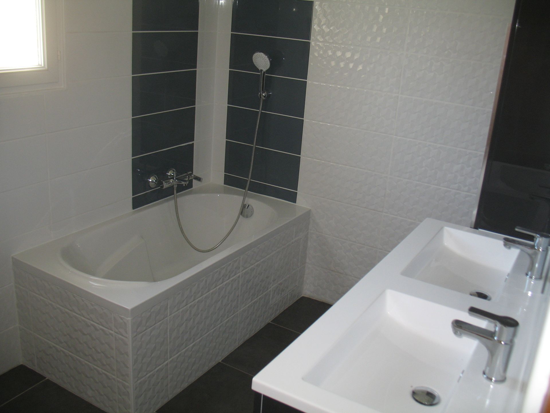 Salle de bain avec baignoire, double vasque et touches de carrelage gris foncé.